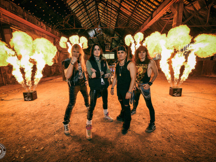 Photo promotionnelle du groupe BlackRain, quatre musiciens devant des jets de flammes dans un hangar