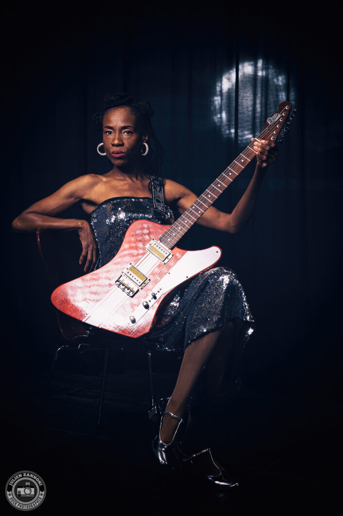 Teneia Sanders lifting her electric guitar during a photoshoot – photo by Julien Zannoni.