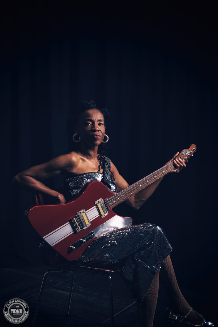 Teneia Sanders seated with her electric guitar during a photoshoot – photo by Julien Zannoni.