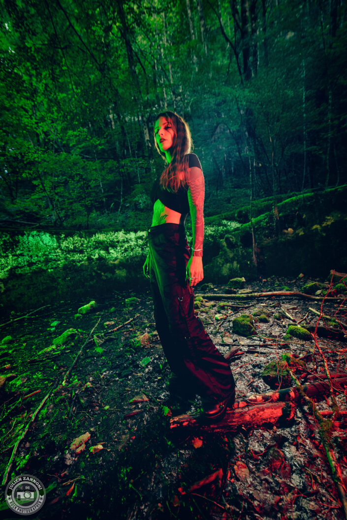 Barbara Mogore, chanteuse de Nightmare, debout dans un bassin abandonné envahi par la végétation, éclairé en vert et rouge.